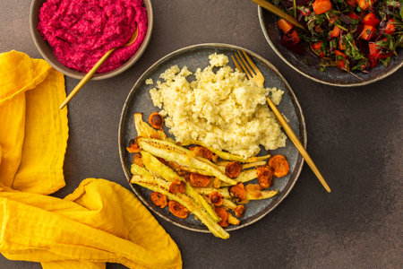 This nutritious meal features millet with baked zucchini and carrots, complemented by a vibrant salad of fresh seasonal vegetables and herbs, alongside chickpea buns and creamy beetroot hummusの写真素材