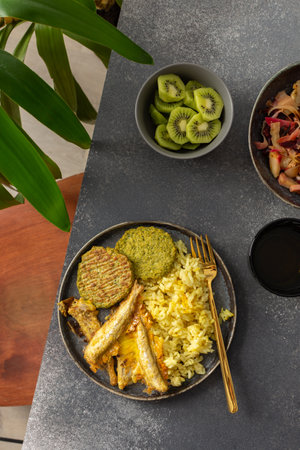 A wholesome breakfast featuring turmeric rice with baked ocean fish, complemented by broccoli pancakes and roasted vegetables, offering a nutritious and satisfying mealの写真素材