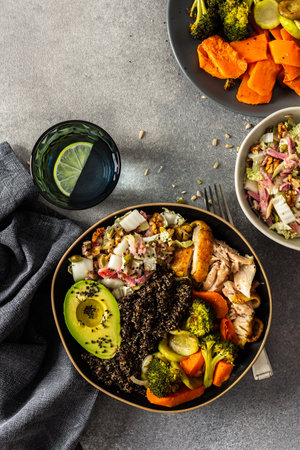 A hearty, balanced breakfast bowl with black quinoa, creamy avocado, roast chicken, sweet potatoes, zucchini, broccoli, and a fresh salad of cabbage and radish with chia and sesame seedsの写真素材