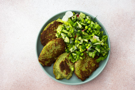 A plate of zucchini and broccoli pancakes alongside a vibrant mixed salad with cucumbers, young peas, and radishes. This healthy vegetarian option is as tasty as it is wholesomeの写真素材