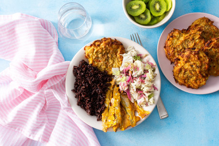 A healthy breakfast featuring brown rice with baked white fish, zucchini-carrot pancakes, cabbage salad with radish, and a refreshing kiwi dessert for a balanced, nutritious start to the dayの写真素材
