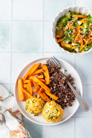 A healthy and filling meal of brown rice, baked sweet potato and squash chickpea pancakes, packed with flavor and nutrients, fresh salad of tomatoes and cucumbers with herbsの写真素材