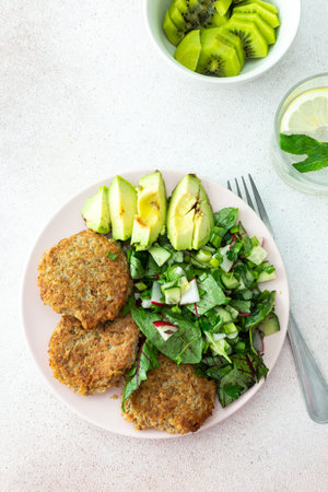 Quinoa cutlets and mixed salad with avocado and radishes, kiwi and water with lemon, delicious hearty breakfasts, vegan lunch plateの写真素材