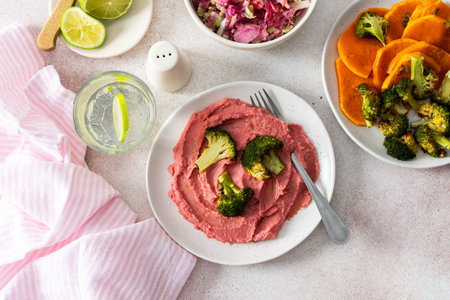 A healthy breakfast with beet hummus, baked sweet potato, and broccoli, topped with a fresh radish and cabbage salad, offering protein and nutrientsの写真素材