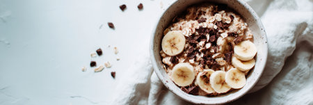 Enjoying a seasonal breakfast of oatmeal topped with banana slices and chocolate bits, served in a quaint kitchen with a relaxed atmosphere in the morning.の素材