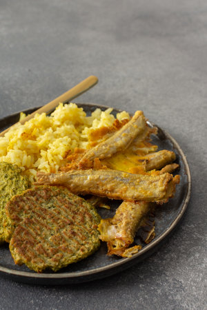 A wholesome breakfast featuring turmeric rice with baked ocean fish, complemented by broccoli pancakes and roasted vegetables, offering a nutritious and satisfying mealの写真素材