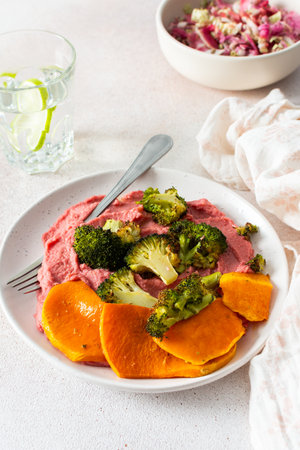 A wholesome breakfast with beet hummus, baked sweet potato, and a fresh radish and cabbage salad, rich in vitamins, fiber, and proteinの写真素材