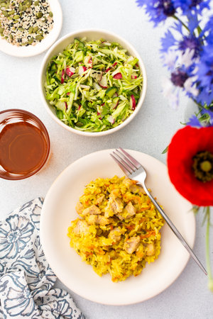 Stewed rice with chicken breast and mixed salad with radishes and various seeds, a served table with food and a vase of flowers, a delicious hearty lunch or dinnerの写真素材