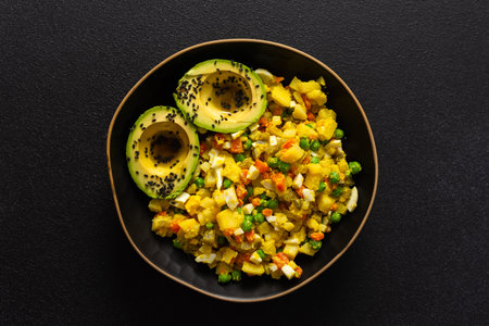 A hearty salad combines boiled egg, chicken breast, vibrant carrots, tender potatoes, green peas, and creamy avocado sprinkled with sesame seeds, all enhanced with olive oil.の写真素材