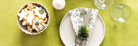 A festive Christmas table setting with an empty plate, cutlery, and napkin on a bright green...