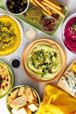 A vibrant charcuterie board features broccoli, turmeric, classic, and beetroot hummus, paired with olives, crackers, and fresh garnishes, perfect for sharing with friendsの写真素材