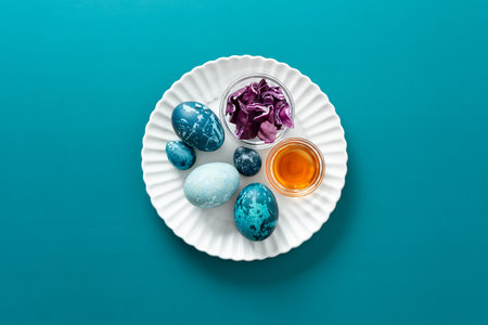 Brightly colored eggs are arranged on a plate alongside natural dye materials like of red cabbage and a small jar of vinegar, celebrating the joy of Easter during spring, how to dye eggs marbled blueの写真素材
