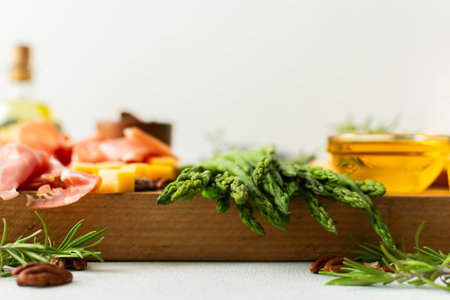 A vibrant charcuterie board is set for a gathering, showcasing fresh asparagus, assorted cheeses, cured meats, and nuts. This setup invites guests to enjoy tasty bites togetherの写真素材
