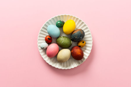 A collection of vibrant Easter eggs in various colors is artfully arranged on a white plate, set...