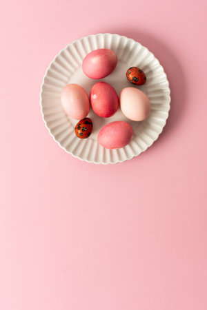 A collection of beautifully dyed Easter eggs in various shades rests on a decorative plate, set against a soft pink background, celebrating the joyful holiday spirit.の写真素材