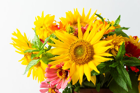 Flowers in a vase fill a space with color and texture. Sunflowers, zinnias, and greenery are mixed together. Light brightens the scene, showcasing their vibrant colors.の写真素材