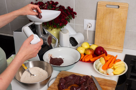 A woman is making liver cutlets in a city kitchen. She is using a grinder to prepare the meat. The...