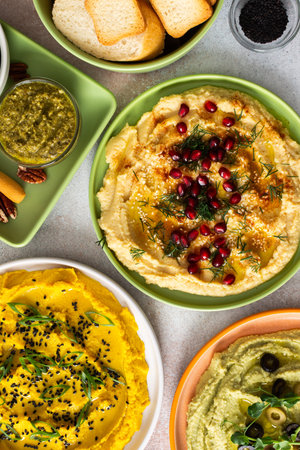 A variety of hummus flavors including turmeric, classic, and broccoli are served with fresh bread, nuts, and garnishes on a colorful charcuterie board, perfect for sharingの写真素材