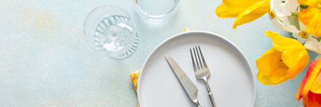 A fresh spring table setting features a plain plate, silver utensils, and a bright yellow napkin....