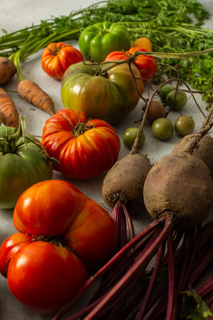 Various types of tomatoes and carrots are placed together on a flat surface. The assortment shows...