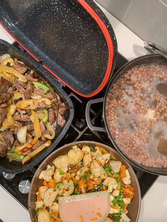 Vegetables are simmering in a pan while meat fries in another. Lentil soup is cooking in a pot,...