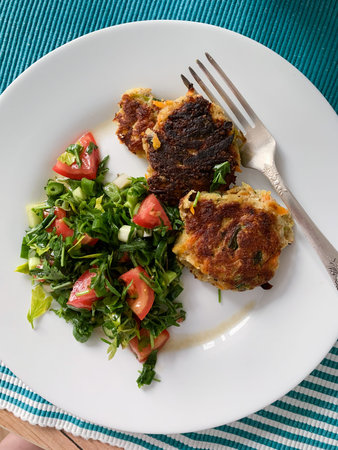 Chicken cutlets are served on a white plate alongside a fresh salad of tomatoes and greens. This meal is prepared for a healthy breakfast or lunch.の写真素材