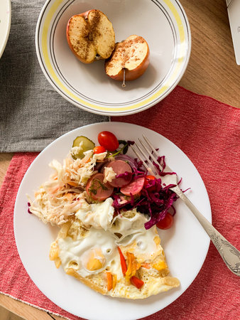 A plate holds an omelet topped with fermented cabbage, tomatoes, radish, and cucumbers alongside a...