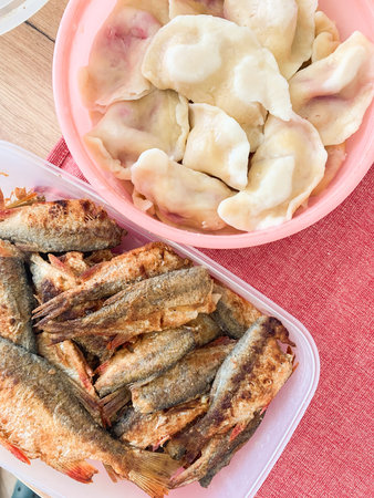 A plate holds fried carp next to a bowl and dumplings with potatoes. This healthy breakfast is prepared for a meal. It features fish and potatoes on a red cloth.の写真素材