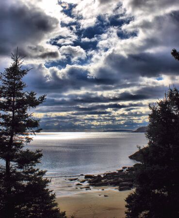 Cloudy day at the beach with sun shimmering on waterの写真素材