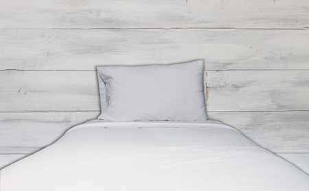 Close up white bedding sheet and pillow with white wooden wall texture backgroundの写真素材