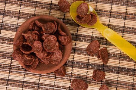 chocolate corn flakes in clay disk with yellow plastic spoonの写真素材