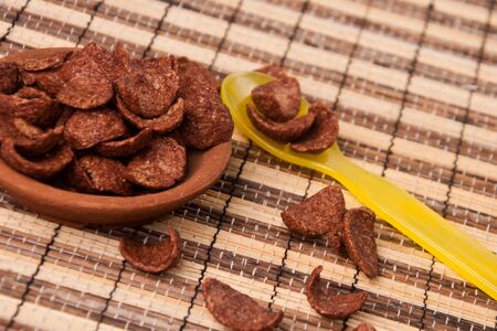 chocolate corn flakes in clay disk with yellow plastic spoonの写真素材