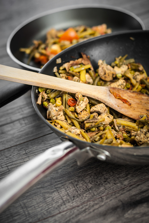 Chicken with vegetables on frying pan. Healthy food. Frying pan with chicken, tomato and other vegetables on wooden table.の写真素材