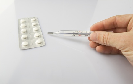 Man's hand with thermometer on white background with  pillsの写真素材