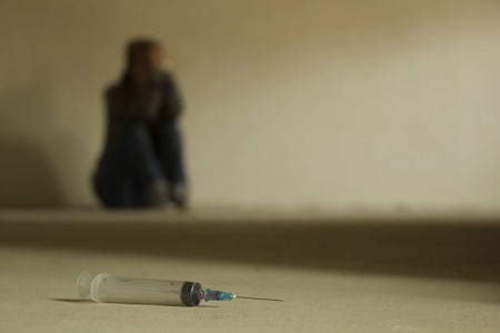 Drug addiction teenager sitting on the cement floor with syringe foregroundの写真素材