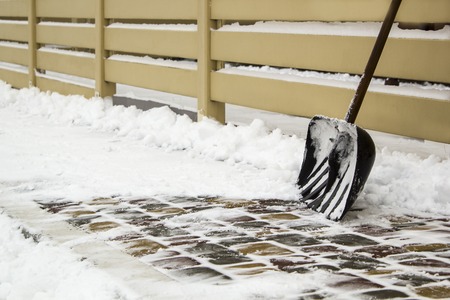 Snow shovel near fence on a snowy road backgroundの写真素材