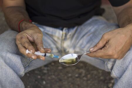 Drug addiction man sitting on the ground with syringe in hands. Anti addiction conceptの写真素材