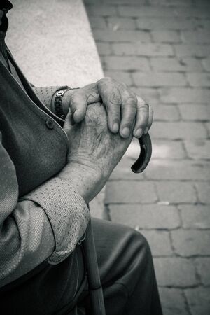 A old man sitting with hands holding his stickの写真素材