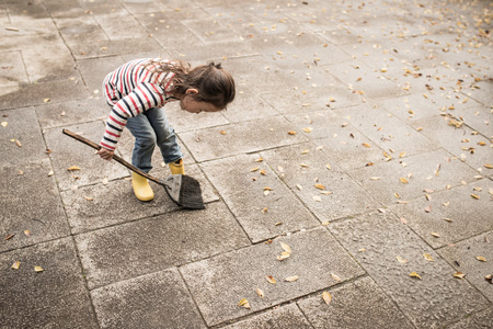 Little girl sweeping up dead leavesの写真素材