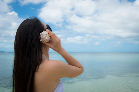 Beautiful woman to listen to the sound of the waves in the shellの写真素材