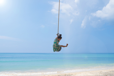Happy little girl swinging at the beautiful blue beachの写真素材