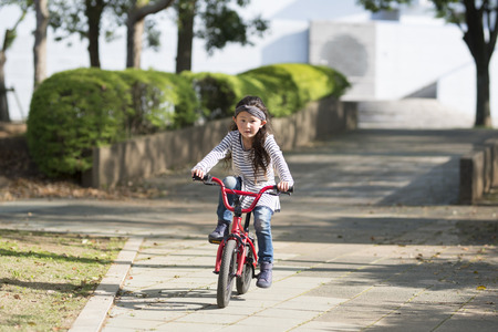Happy little girl riding on a red bicycle in the parkの写真素材