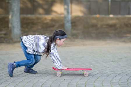 Pretty little girl playing with a red skateboardの写真素材