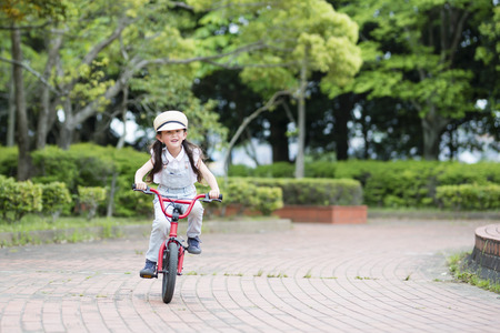 Happy little girl riding on a red bicycle on the pathの写真素材