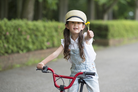 Portrait of a pretty little girl smiling happily posing relaxed with her bicycle outdoors holding some flowersの写真素材