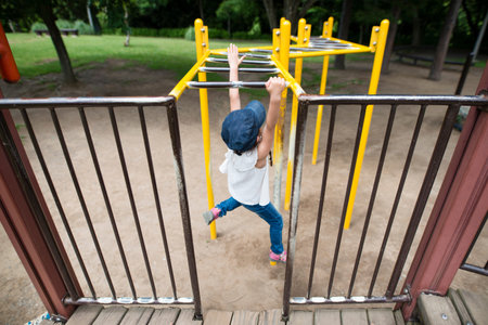 Little preschool girl hanging on the monkey bars at park