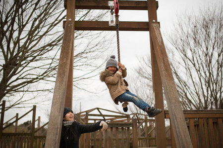 Happy little girl playing with rope swing on playground on cold day