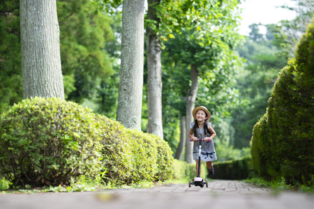 Happy little girl riding on kick scooter in the parkの写真素材