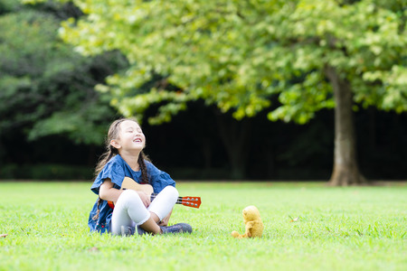 Cute little girl playing a guitar on the green grassの写真素材