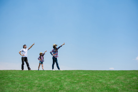 Father and mother and daughter pointing to the sky in the meadowの販売画像